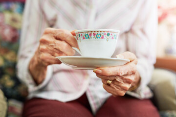 Hands, tea cup and senior woman in house for relax, comfort and afternoon warm beverage. Home,...