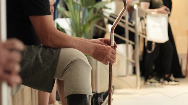 Man with prosthetic leg sits and holds his cane.