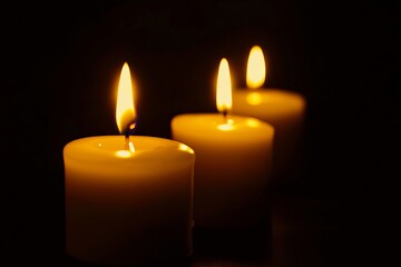 Three white candles are lit in the dark
