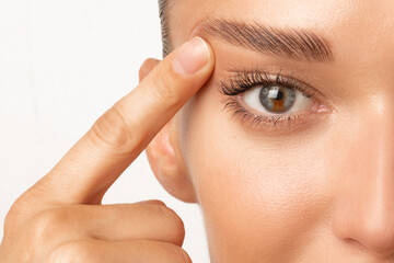Blepharoplasty. Woman with unusual eye color touching eyelid skin and pointing to the wrinkles on...