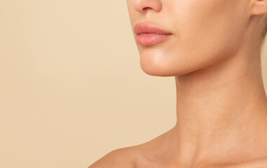 Woman with tender female neck, lips and chin posing isolated over beige studio background, free...