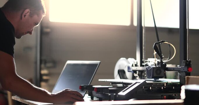 An engineer is creating a prototype of a component using a 3D printer. The focus is on the printing head, and the engineer is working on a laptop in a CAD program.