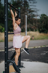 Woman hanging on an outdoor exercise bar, showcasing fitness and strength during her workout in a natural park setting.