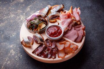 Snacks on wooden utensils. Sliced bacon and hunting sausages. Small snacks for beer in the form of fish on bread. Food on a dark texture background.