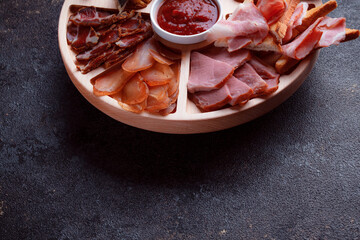 Snacks on wooden utensils. Sliced bacon and hunting sausages. Small snacks for beer in the form of fish on bread. Food on a dark texture background.