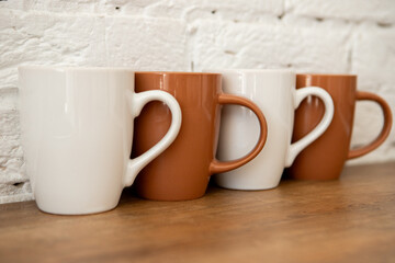 brown and white cups stand on a wooden table near a white wall