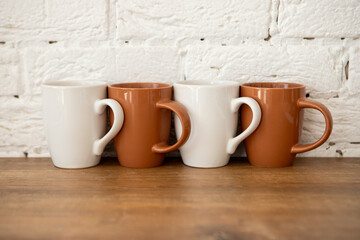 brown and white cups stand on a wooden table near a white wall