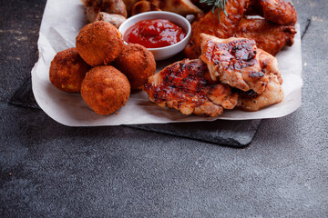 Original serving of meat dishes. Crispy fried chicken wings and thighs. Breaded cheese balls and grilled sausages with rosemary and ketchup. Food for outdoor catering.