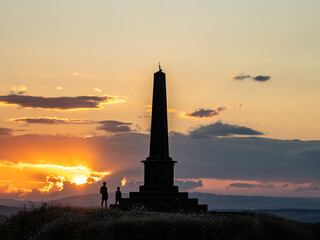 Two people watching sunset behind monument on hilltop