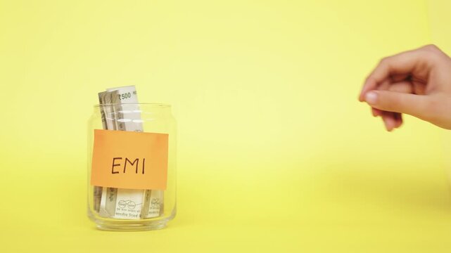 Saving money for EMI. Putting Indian Rupee notes into the glass jar