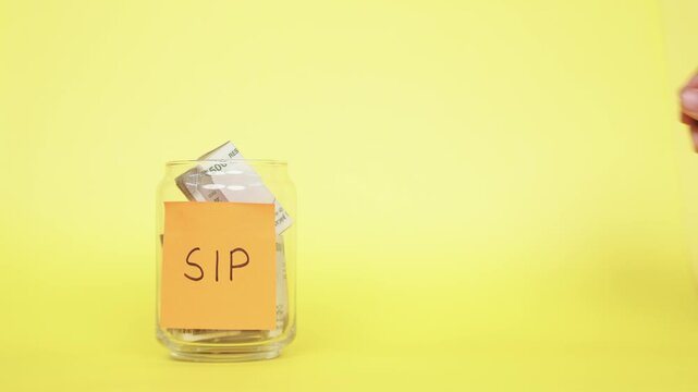 Saving money for SIP. Putting Indian Rupee notes into the glass jar