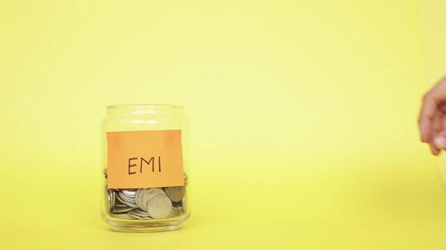 Saving money for EMI. Putting Indian Rupee coins into the glass jar