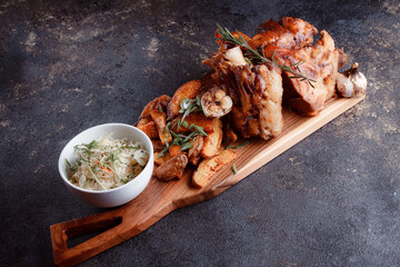 A set dish: a large fried piece of meat on the bone, country-style grilled potatoes, a mini salad of cabbage, bean sprouts, chia seeds and green onions. Original serving on a wooden cutting board.