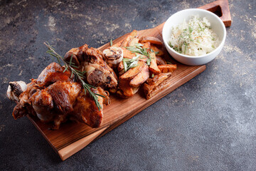 A set dish: a large fried piece of meat on the bone, country-style grilled potatoes, a mini salad of cabbage, bean sprouts, chia seeds and green onions. Original serving on a wooden cutting board.
