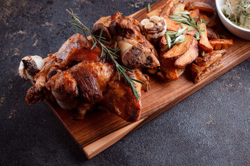 A set dish: a large fried piece of meat on the bone, country-style grilled potatoes, a mini salad of cabbage, bean sprouts, chia seeds and green onions. Original serving on a wooden cutting board.