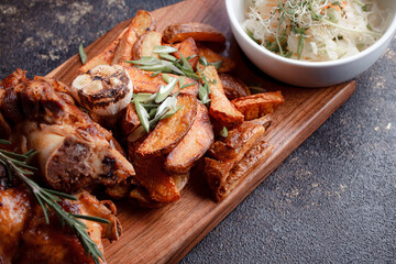 A set dish: a large fried piece of meat on the bone, country-style grilled potatoes, a mini salad of cabbage, bean sprouts, chia seeds and green onions. Original serving on a wooden cutting board.