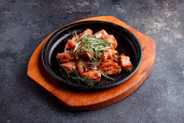 Hot frying pan with pieces of fried meat in caramelized sauce. Cooked and fresh vegetables as garnish and garnish.