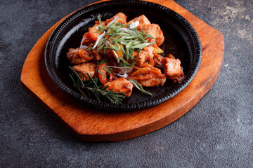 Hot frying pan with pieces of fried meat in caramelized sauce. Cooked and fresh vegetables as garnish and garnish.