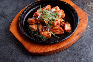Hot frying pan with pieces of fried meat in caramelized sauce. Cooked and fresh vegetables as garnish and garnish.