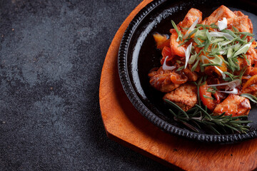Hot frying pan with pieces of fried meat in caramelized sauce. Cooked and fresh vegetables as garnish and garnish.