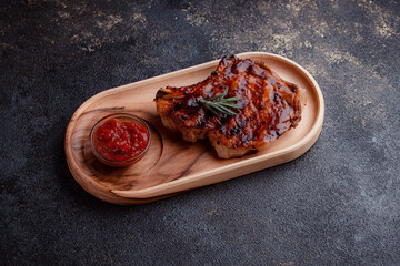 Grilled pork steak in caramelized sauce. Serving meat on eco-friendly wooden utensils. A sprig of fresh rosemary and tomato sauce.