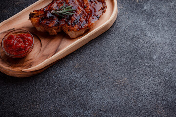 Grilled pork steak in caramelized sauce. Serving meat on eco-friendly wooden utensils. A sprig of fresh rosemary and tomato sauce.