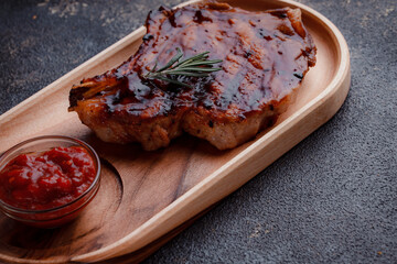 Grilled pork steak in caramelized sauce. Serving meat on eco-friendly wooden utensils. A sprig of fresh rosemary and tomato sauce.