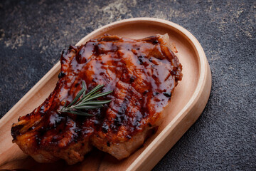 Grilled pork steak in caramelized sauce. Serving meat on eco-friendly wooden utensils. A sprig of fresh rosemary and tomato sauce.