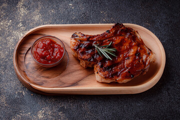 Grilled pork steak in caramelized sauce. Serving meat on eco-friendly wooden utensils. A sprig of fresh rosemary and tomato sauce.