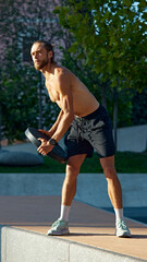 Obraz premium Early morning workout. Shirtless muscular man training in public park, doing exercises with heavy weights. Discipline and motivation. Concept of sport, active and healthy lifestyle, fitness