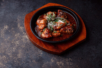 Hot frying pan with pieces of fried meat in caramelized sauce. Cooked and fresh vegetables as garnish and garnish.  A dish with the addition of flax seeds and sesame seeds.