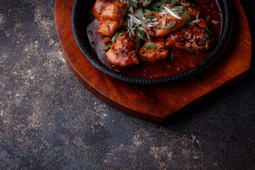 Hot frying pan with pieces of fried meat in caramelized sauce. Cooked and fresh vegetables as garnish and garnish.  A dish with the addition of flax seeds and sesame seeds.