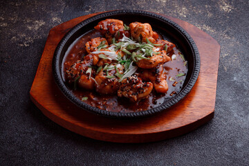 Hot frying pan with pieces of fried meat in caramelized sauce. Cooked and fresh vegetables as garnish and garnish.  A dish with the addition of flax seeds and sesame seeds.