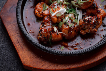 Hot frying pan with pieces of fried meat in caramelized sauce. Cooked and fresh vegetables as garnish and garnish.  A dish with the addition of flax seeds and sesame seeds.