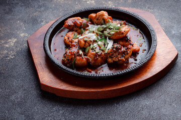 Hot frying pan with pieces of fried meat in caramelized sauce. Cooked and fresh vegetables as garnish and garnish.  A dish with the addition of flax seeds and sesame seeds.