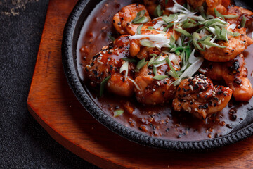 Hot frying pan with pieces of fried meat in caramelized sauce. Cooked and fresh vegetables as garnish and garnish.  A dish with the addition of flax seeds and sesame seeds.