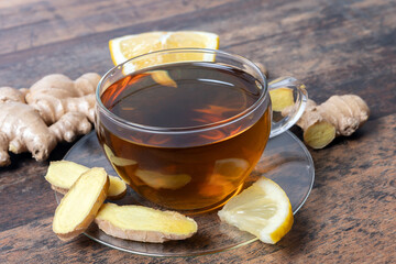 Ginger tee on wooden table, surrounded by sliced lemon and ginger root in  transparent tea cup,