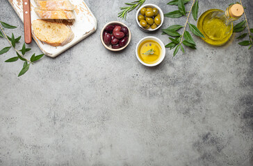 Composition with sliced fresh ciabatta on cutting board, green and brown olives, olive oil with...