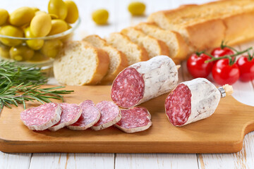Traditional Spanish fuet spicy pork dry cured salami sausage with rosemary and baguet on a wooden table.