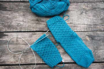 Blue yarn ball with knitted sock and knitting needles. Blue knitting wool on grunge wooden background. Woven crochet close up. Knitting hobby. Knitwear concept. Needlework background. Handmade clothes
