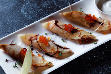 Set of pancakes with red salmon caviar. Beautiful serving of the dish on a textured dark blue background. Restaurant dessert menu.