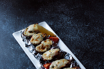 Boiled oysters with melted cheese. Nice serving of oysters on a large white platter. Seafood prepared for a restaurant on a dark blue background.