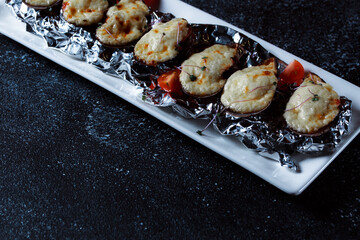 Boiled oysters with melted cheese. Nice serving of oysters on a large white platter. Seafood prepared for a restaurant on a dark blue background.