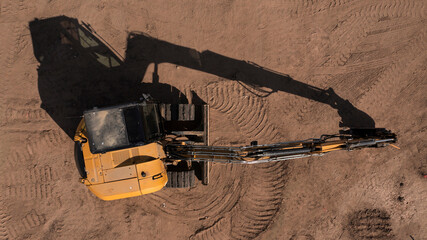 Aerial straight down view of an excavator on a leveled job site with tread tracks in the sand. © Matt Gush