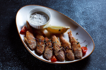 King fish on a large white dish. Fish fried in batter with a beautiful presentation. Cooked seafood on a dark blue background.