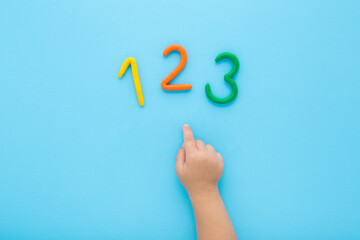 Baby boy hand finger pointing to colorful 123 numbers created from modeling clay on light blue...