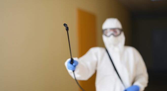 Disinfection specialist in protective uniform with a spray bottle, close-up, blurry. Deratization, deodorization service