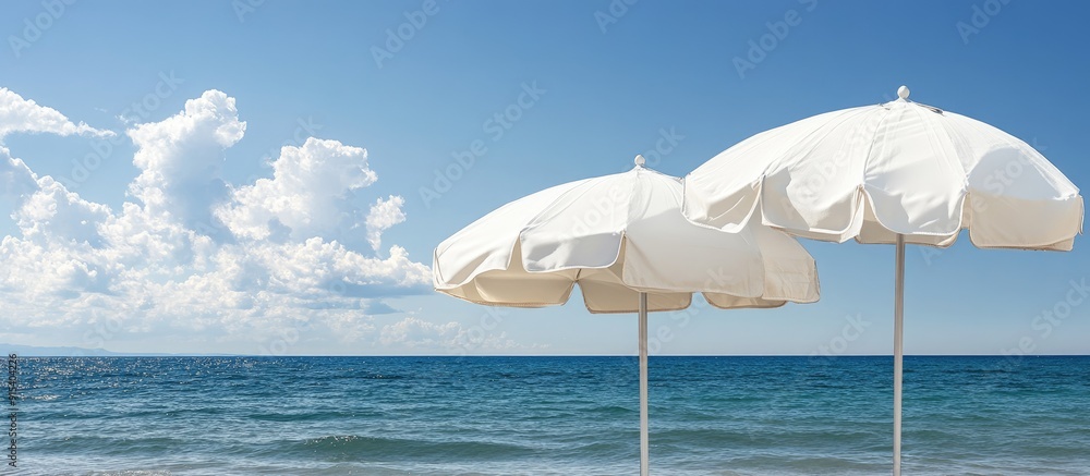Poster Close up of two closed white canvas beach umbrellas set against a backdrop of the sea and a blue sky with clouds. with copy space image. Place for adding text or design