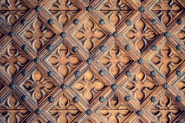 An exquisitely carved wooden door displays a complex diamond pattern and floral designs that highlight traditional woodworking artistry.