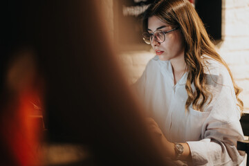 Young businesswoman focused on work in a dimly lit office, wearing glasses and a white shirt, late evening.